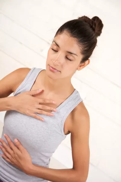 A woman with her eyes closed, one hand on stomach and one hand on heart.