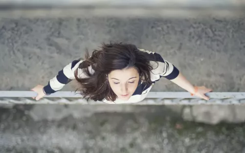 Woman standing on the edge of a bridge railing, leaning her head back to the sky.
