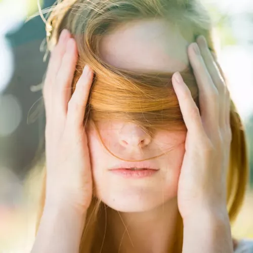 A white woman covers her eyes and face with a section of her hair.