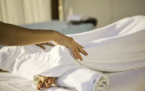 A therapist lightly touches a prone client's back of the feet, with the legs and feet fully draped.
