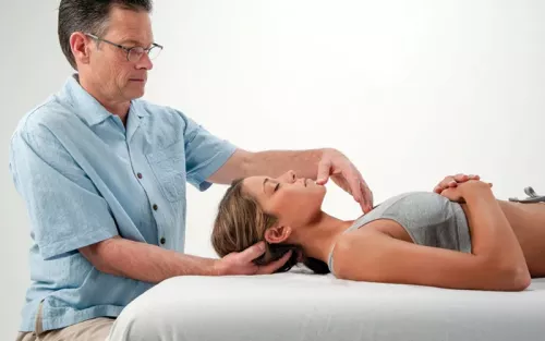 Til Luchau works with a client supine on a table, using extremely light touch to the client's head and neck.