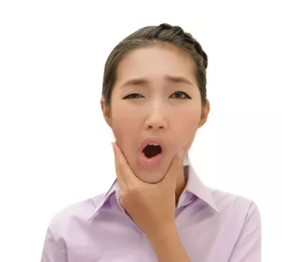 An Asian woman rubbing her jaw with her mouth open.