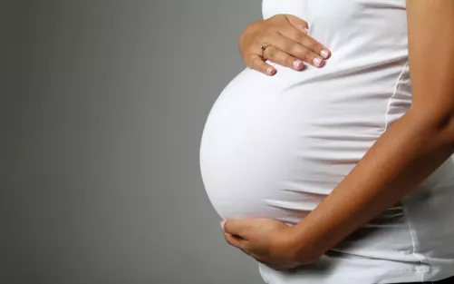 A pregnant woman in a white dress holding her bump.