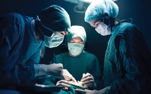 Three surgeons in masks and surgical attire looking down at a patient's incision.