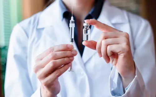 A medical professional holding a metal syringe and vial of clear medicine.