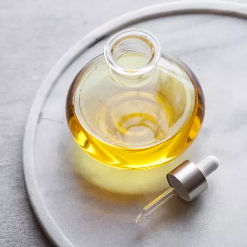 A clear glass jar of massage oil with a dropper next to it.
