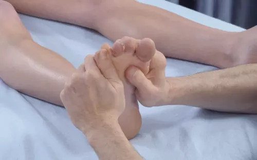 A therapist uses two hands on a client's right foot to perform a metatarsal spreading technique.
