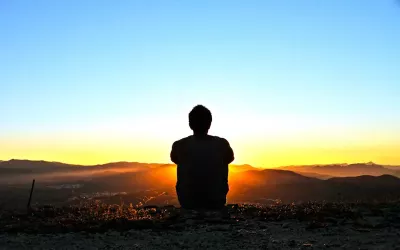 A person sitting on the ground outside watching a vibrant colorful sunset.