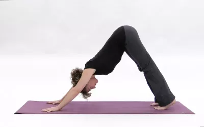 A woman straightens her back legs and moves into downward dog yoga pose.
