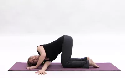 A woman with knees bent on her yoga mat, raising her right arm and threading it through to her left side, creating tension.