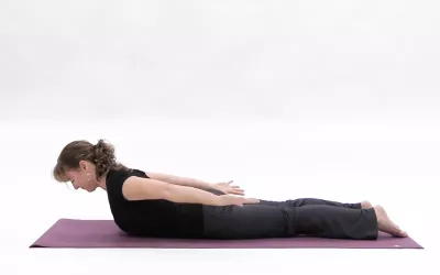 A woman belly down on a yoga mat, her head and chest lifted up.