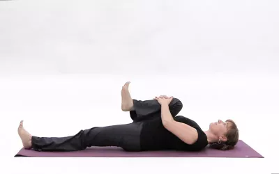 A woman holding and pulling one knee in towards her chest as she lies on her back.