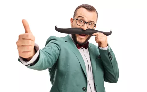 Man in a blazer and bowtie holding a large costume moustache over his face.
