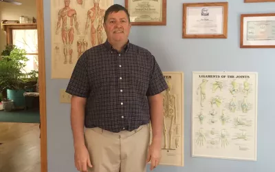 Dan Rupp stands next to anatomy posters in his massage business space.