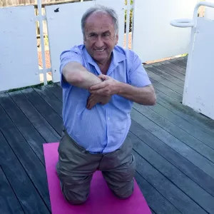 The author kneeling on a yoga mat, stretching his right elbow forward to test for flexibility.