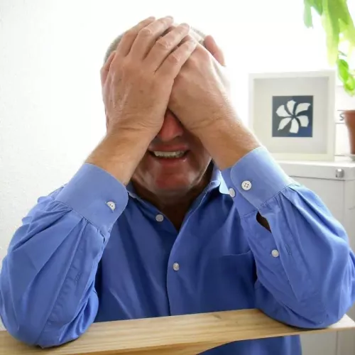 The author in a blue button-down shirt using both hands to cover his eyes.
