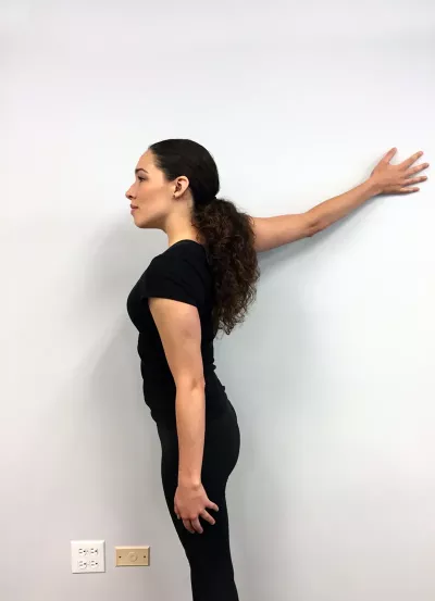 A woman with her right arm in outward flexion pushing against a wall.
