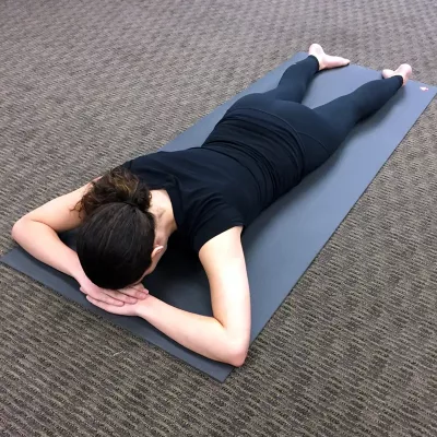 A woman with her forehead resting on the backs of her hands, laying face down in the crocodile pose.