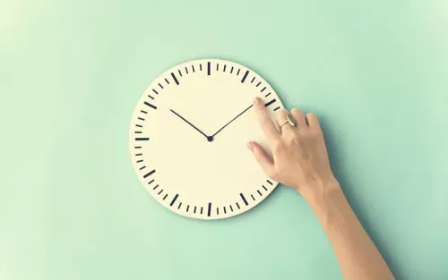 A hand pointing to the minute hand on an analog clock.