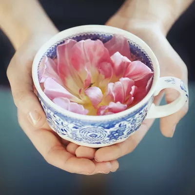 Two hands cradling a ceramic teacup full of flower petals.