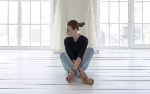A woman sitting criss-cross with her legs pulled in towards her body.