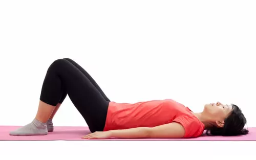Woman lying on her back on a yoga mat with knees bent.