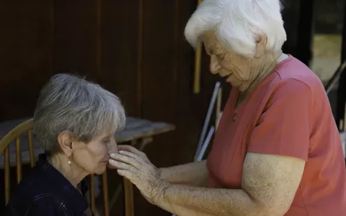 Dolores Krieger in her 90s practicing and providing therapeutic touch to a seated woman.