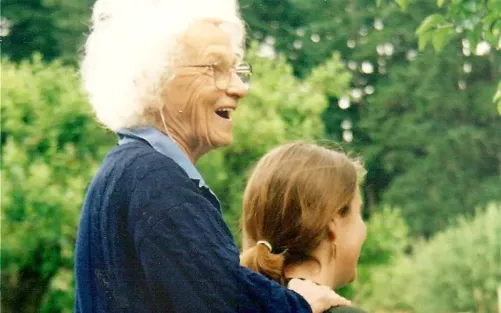 Dora Kunz with poofy white hair smiling while laying on hands.
