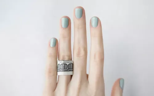 A left manicured hand with a $100 bill on the ring finger.