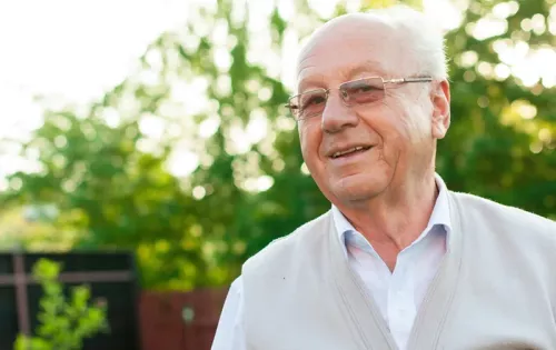An older man smiling slightly, standing outside.