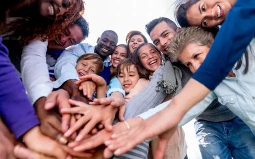 A group of people of all different ages and ethnicities put their hands together in a circle for a team huddle.