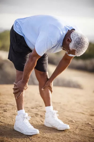 An African American man in running attire bent over looking tired.