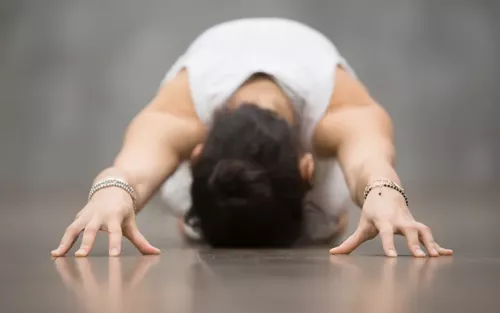 A person in a tank top folded over on the floor in child's pose, head down.