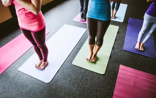 People in colorful clothes stand on a rainbow of yoga mats.