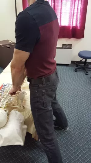 The therapist demonstrates how to lean forward into the table slightly, locking the knees with the shoulders stacked above them.