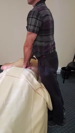 A therapist locking his back leg, approaching the client from the side of the table.