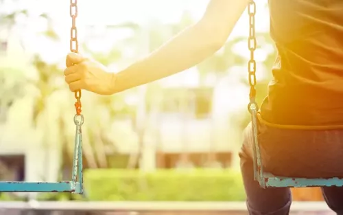 Person sitting on a swing holding the chains of both swings on a sunny day.