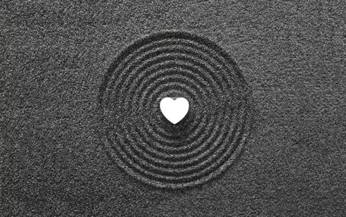 Many concentric circles drawn in grey sand with a white heart in the center.