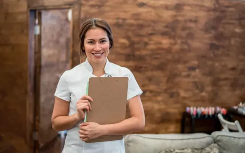 A woman in an office smiling and holding a clipboard.