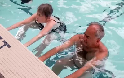 Two people in a pool with their feet and arms reached out, touching the pool wall.
