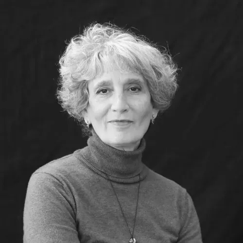 Vered, an older woman with short choppy hair in a sweater, smiling slightly at the camera.