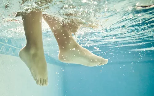 Two legs kick and splash through the water near the surface of a pool.