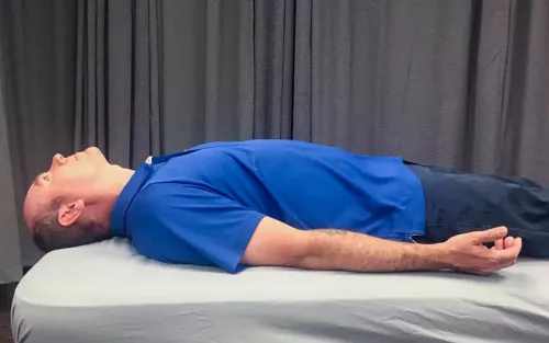A man in a blue shirt lies flat on a massage table.