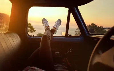 A person hanging their feet out a car window at sunset.