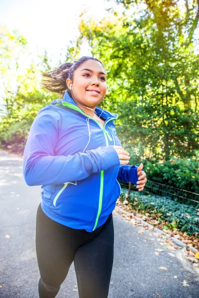 A woman running in a bright blue jacket and wire headphones.
