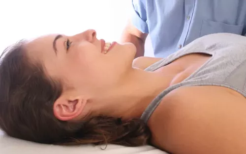 A woman lying supine on a table in a tank top, smiling.