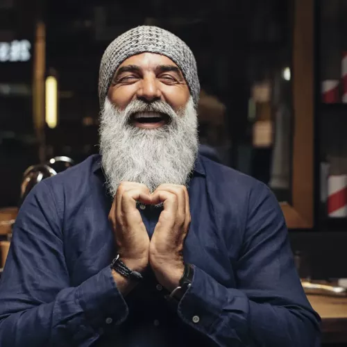 A man with a full gray beard clasps his hands together and laughs.