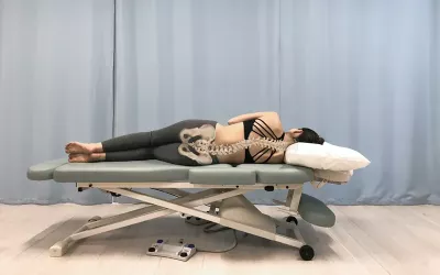 A woman with an S-curve spine sidelying flat on a massage table.