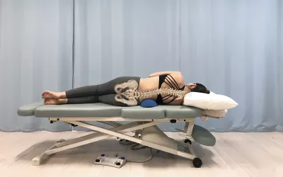 A woman with an S-curve spine sidelying over a bolster on a table.
