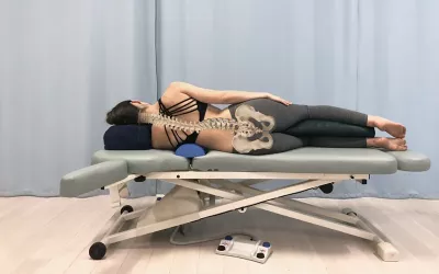 A client side-lying on their left side with bolster placed under apex of thoracic scoliotic curve.